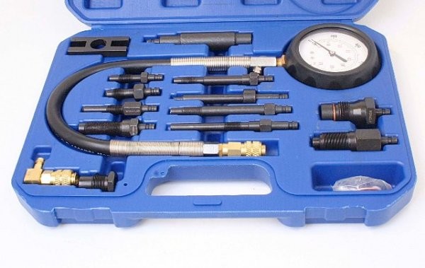Close-up of diesel compression tester components: pressure gauge, threaded adapters, braided hose with brass connector and spare seals in blue molded case